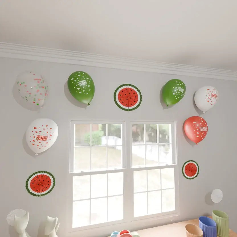 Ramadan Mubarak latex balloons and watermelon paper fans stuck to a wall beside two windows