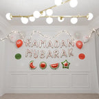 White watermelon-print Ramadan Mubarak foil balloons on a white wall with string lights and red balloons