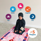 Child in a black hijab and abaya kneeling on the Kids Interactive Prayer Mat (Pink), with icons for the five daily prayers